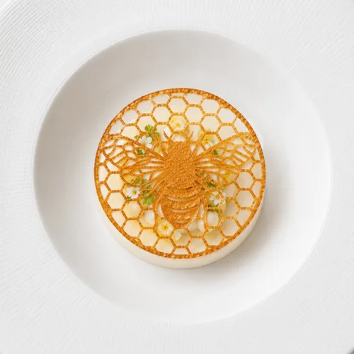 Bee tuile dessert garnish resting above white mousse with meringue and edible flowers on a fine dining plated dessert