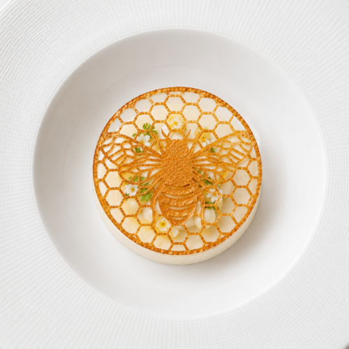 Bee tuile dessert garnish resting above white mousse with meringue and edible flowers on a fine dining plated dessert