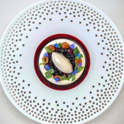 Gourmet dessert with berries and decorative flowers.
