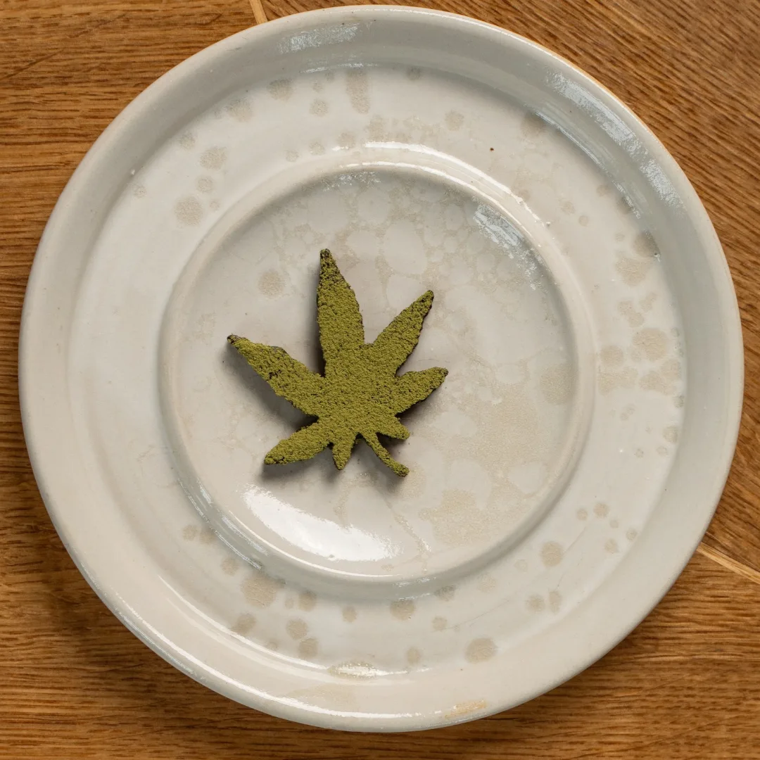 Malt tuile shaped as a hemp leaf with cream and hemp powder on a plate