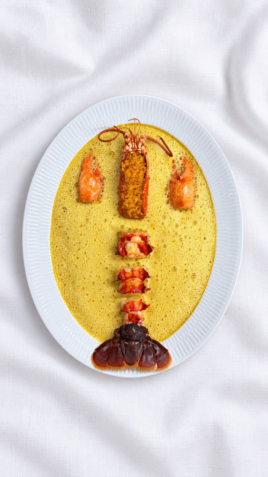 Lobster served with saffron lobster sauce on an oval white plate and white tablecloth, by August Theil